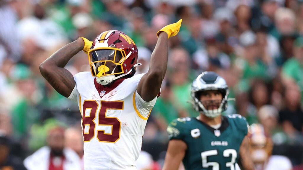 Washington Commanders tight end Chig Okonkwo signals a first down with one arm raised and the other flexed behind his helmet.