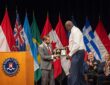 Shaquille O'Neal accepts a framed plaque on stage at an FBI ceremony as seated officials applaud.